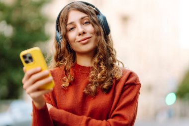 Sokakta yürürken müzik dinleyen genç bir kadın. Seyahat, turizm, teknoloji, blog konsepti