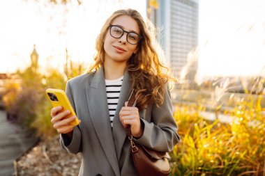 Şehirde gülümseyen ve cep telefonu kullanan mutlu öğrenci kadın. Yaşam tarzı, seyahat, turizm, teknoloji, blog yazma, iletişim kavramı