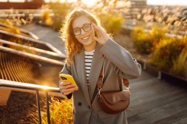 Şehirde gülümseyen ve cep telefonu kullanan mutlu öğrenci kadın. Yaşam tarzı, seyahat, turizm, teknoloji, blog yazma, iletişim kavramı