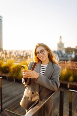 Şehirde gülümseyen ve cep telefonu kullanan mutlu öğrenci kadın. Yaşam tarzı, seyahat, turizm, teknoloji, blog yazma, iletişim kavramı