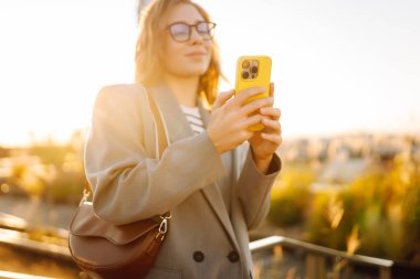 Şehirde gülümseyen ve cep telefonu kullanan mutlu öğrenci kadın. Yaşam tarzı, seyahat, turizm, teknoloji, blog yazma, iletişim kavramı