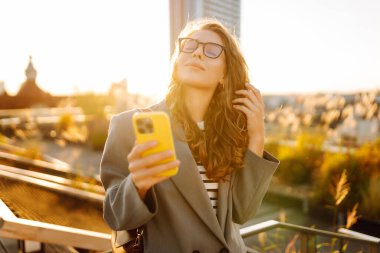 Şehirde gülümseyen ve cep telefonu kullanan mutlu öğrenci kadın. Yaşam tarzı, seyahat, turizm, teknoloji, blog yazma, iletişim kavramı