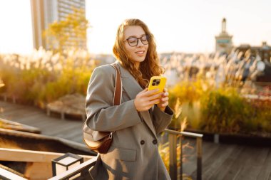 Şehirde gülümseyen ve cep telefonu kullanan mutlu öğrenci kadın. Yaşam tarzı, seyahat, turizm, teknoloji, blog yazma, iletişim kavramı