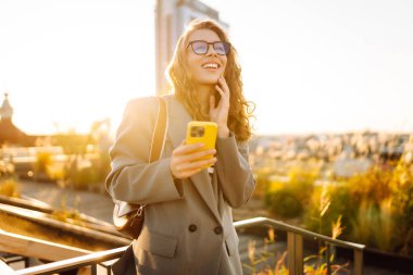 Şehirde gülümseyen ve cep telefonu kullanan mutlu öğrenci kadın. Yaşam tarzı, seyahat, turizm, teknoloji, blog yazma, iletişim kavramı