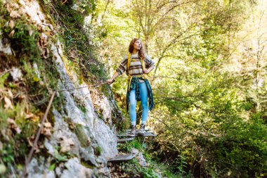 Kadın turist yazın doğayı keşfediyor, köprüde yürüyor. Ormanlarda dolaşan büyük sırt çantalı bir yürüyüşçü. Etkin yaşam biçimi