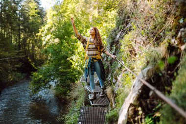 Kadın turist yazın doğayı keşfediyor, köprüde yürüyor. Ormanlarda dolaşan büyük sırt çantalı bir yürüyüşçü. Etkin yaşam biçimi