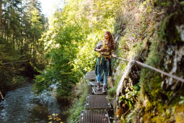 Kadın turist yazın doğayı keşfediyor, köprüde yürüyor. Ormanlarda dolaşan büyük sırt çantalı bir yürüyüşçü. Etkin yaşam biçimi