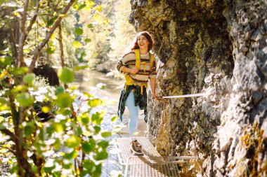 Kadın turist yazın doğayı keşfediyor, köprüde yürüyor. Ormanlarda dolaşan büyük sırt çantalı bir yürüyüşçü. Etkin yaşam biçimi