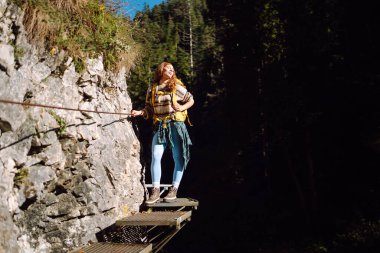 Kadın turist yazın doğayı keşfediyor, köprüde yürüyor. Ormanlarda dolaşan büyük sırt çantalı bir yürüyüşçü. Etkin yaşam biçimi