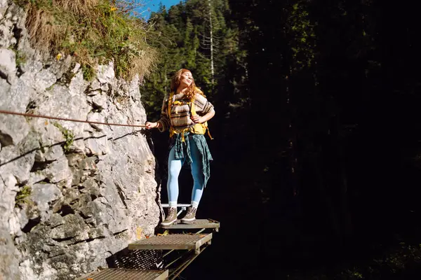 Kadın turist yazın doğayı keşfediyor, köprüde yürüyor. Ormanlarda dolaşan büyük sırt çantalı bir yürüyüşçü. Etkin yaşam biçimi