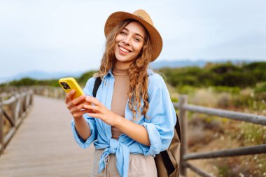 Mutlu kadın akıllı telefon kullanıyor ve deniz kenarında güneşli bir gezinti güvertesinde gülümsüyor. Boş zaman, açık hava ve doğaya yakın. Avrupa seyahati