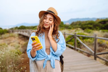 Mutlu kadın akıllı telefon kullanıyor ve deniz kenarında güneşli bir gezinti güvertesinde gülümsüyor. Boş zaman, açık hava ve doğaya yakın. Avrupa seyahati
