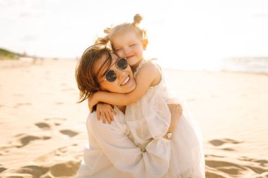 Gülümseyen anne ve güzel kız gün batımında kumsalda eğleniyorlar. Çocukluk, eğlence, rahatlama konsepti