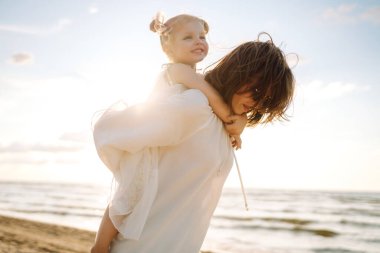 Gülümseyen anne ve güzel kız gün batımında kumsalda eğleniyorlar. Çocukluk, eğlence, rahatlama konsepti