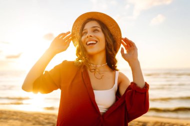 Şapkalı, kollarını havaya kaldırmış, sıcak yaz gününde plaj okyanusunu seyreden mutlu genç bir kadın. Seyahat, hafta sonu, rahatlama ve yaşam tarzı konsepti