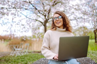 Parkta dizüstü bilgisayarda çalışan çekici bir kadın. Uzaktan kumanda. İş, blog yazma, serbest çalışma kavramı