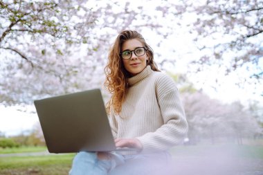 Parkta dizüstü bilgisayarda çalışan çekici bir kadın. Uzaktan kumanda. İş, blog yazma, serbest çalışma kavramı