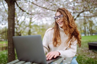Parkta dizüstü bilgisayarda çalışan çekici bir kadın. Uzaktan kumanda. İş, blog yazma, serbest çalışma kavramı