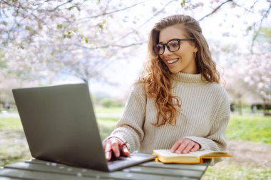 Parkta dizüstü bilgisayarda çalışan çekici bir kadın. Uzaktan kumanda. İş, blog yazma, serbest çalışma kavramı