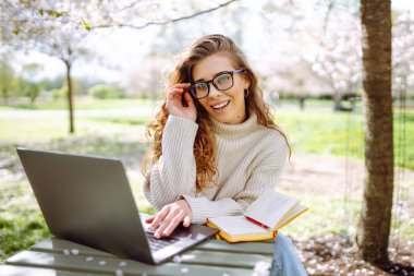 Parkta dizüstü bilgisayarda çalışan çekici bir kadın. Uzaktan kumanda. İş, blog yazma, serbest çalışma kavramı