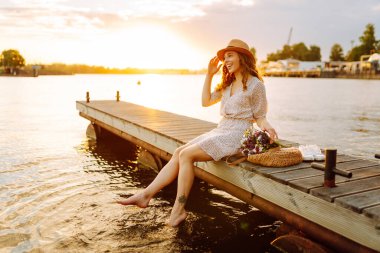 Bir buket yabani çiçekle mutlu genç gün batımında nehirde bir köprüde yürüyor. Düğünün kırsal tarzı.