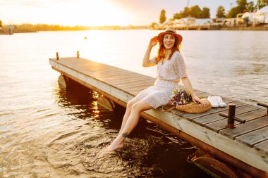 Bir buket yabani çiçekle mutlu genç gün batımında nehirde bir köprüde yürüyor. Düğünün kırsal tarzı.