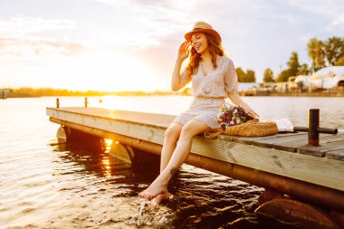 Bir buket yabani çiçekle mutlu genç gün batımında nehirde bir köprüde yürüyor. Düğünün kırsal tarzı.