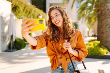 Mutlu kadın yolda yürürken akıllı telefon kamerasıyla selfie çekiyor. Seyahat günlüğü