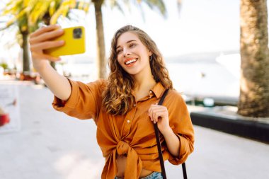 Mutlu kadın yolda yürürken akıllı telefon kamerasıyla selfie çekiyor. Seyahat günlüğü