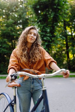 Güneşli bir parkta bisiklet süren genç ve güzel bir kadın. Turist parkta eğleniyor, yürüyüş yapıyor. Eğlence anlayışı, yürüyüş. Etkin yaşam biçimi.
