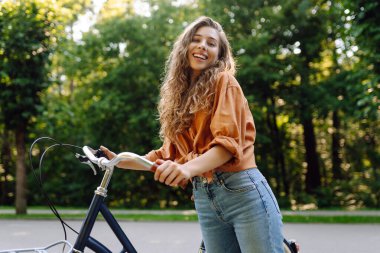 Güneşli bir parkta bisiklet süren genç ve güzel bir kadın. Turist parkta eğleniyor, yürüyüş yapıyor. Eğlence anlayışı, yürüyüş. Etkin yaşam biçimi.