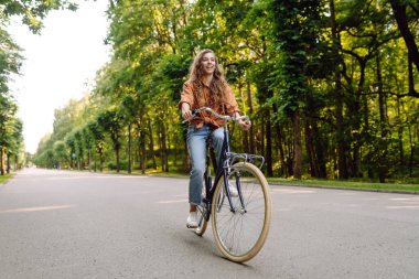 Güneşli bir parkta bisiklet süren genç ve güzel bir kadın. Turist parkta eğleniyor, yürüyüş yapıyor. Eğlence anlayışı, yürüyüş. Etkin yaşam biçimi.