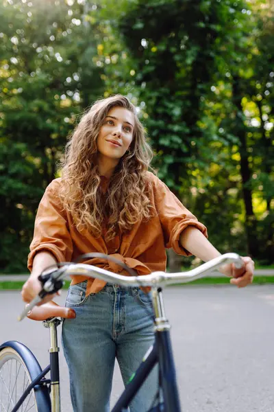 Güneşli bir parkta bisiklet süren genç ve güzel bir kadın. Turist parkta eğleniyor, yürüyüş yapıyor. Eğlence anlayışı, yürüyüş. Etkin yaşam biçimi.