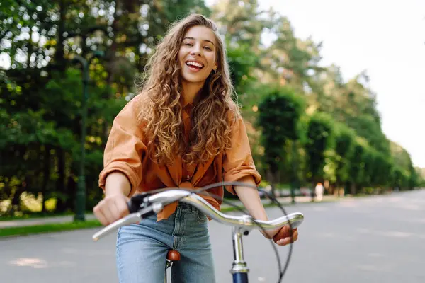 Güneşli bir parkta bisiklet süren genç ve güzel bir kadın. Turist parkta eğleniyor, yürüyüş yapıyor. Eğlence anlayışı, yürüyüş. Etkin yaşam biçimi.