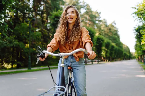 Güneşli bir parkta bisiklet süren genç ve güzel bir kadın. Turist parkta eğleniyor, yürüyüş yapıyor. Eğlence anlayışı, yürüyüş. Etkin yaşam biçimi.