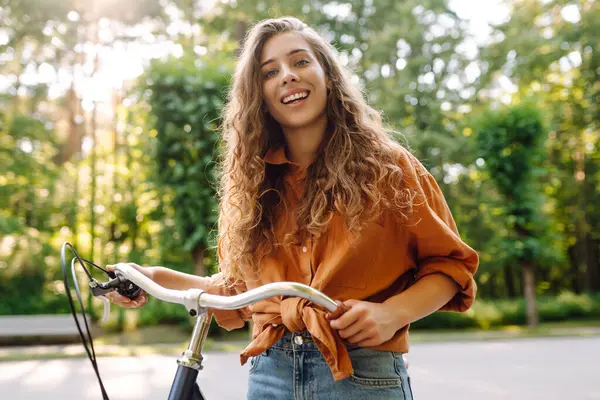 Güneşli bir parkta bisiklet süren genç ve güzel bir kadın. Turist parkta eğleniyor, yürüyüş yapıyor. Eğlence anlayışı, yürüyüş. Etkin yaşam biçimi.