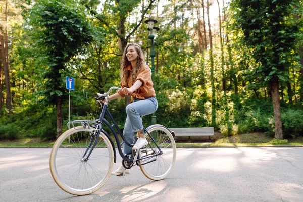 Güneşli bir parkta bisiklet süren genç ve güzel bir kadın. Turist parkta eğleniyor, yürüyüş yapıyor. Eğlence anlayışı, yürüyüş. Etkin yaşam biçimi.