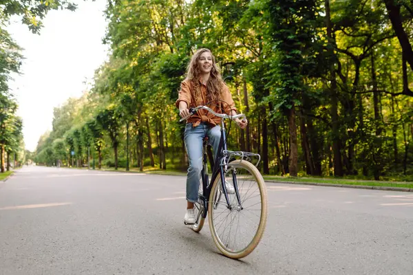 Güneşli bir parkta bisiklet süren genç ve güzel bir kadın. Turist parkta eğleniyor, yürüyüş yapıyor. Eğlence anlayışı, yürüyüş. Etkin yaşam biçimi.