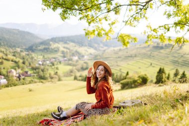 Şapkalı güzel kadın gün batımında Yeşil Tepe 'den manzaranın tadını çıkarıyor. Genç bayan gezgin rahatlar ve manzara karşısında özgürlüğünü hisseder. Seyahat, eğlence, yürüyüş konsepti.