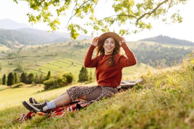 Şapkalı güzel kadın gün batımında Yeşil Tepe 'den manzaranın tadını çıkarıyor. Genç bayan gezgin rahatlar ve manzara karşısında özgürlüğünü hisseder. Seyahat, eğlence, yürüyüş konsepti.