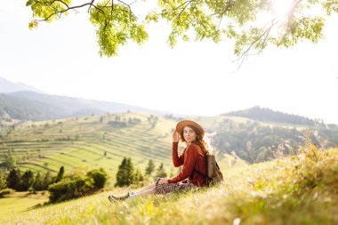 Şapkalı güzel kadın gün batımında Yeşil Tepe 'den manzaranın tadını çıkarıyor. Genç bayan gezgin rahatlar ve manzara karşısında özgürlüğünü hisseder. Seyahat, eğlence, yürüyüş konsepti.