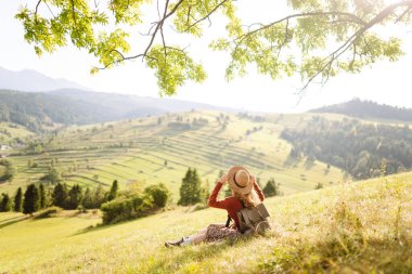 Şapkalı güzel kadın gün batımında Yeşil Tepe 'den manzaranın tadını çıkarıyor. Genç bayan gezgin rahatlar ve manzara karşısında özgürlüğünü hisseder. Seyahat, eğlence, yürüyüş konsepti.