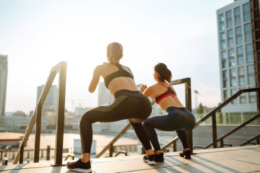 Spor giyimli iki kadın dışarıda birlikte egzersiz yapıyor. Çatıda egzersiz yapan güzel bir kadın. Spor anlayışı, aktivite. Yaşam biçimi.
