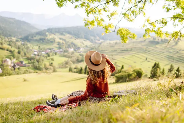 Şapkalı güzel kadın gün batımında Yeşil Tepe 'den manzaranın tadını çıkarıyor. Genç bayan gezgin rahatlar ve manzara karşısında özgürlüğünü hisseder. Seyahat, eğlence, yürüyüş konsepti.