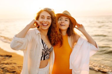 İki genç bayan arkadaş gün batımı kumsalında eğleniyor, birlikte vakit geçiriyorlar. Güzel kadınlar denizde sıcak bir günbatımının tadını çıkarıyorlar. Arkadaşlık, rahatlama konsepti..