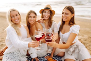 Mutlu kız arkadaşlar gün batımı kumsalında birlikte vakit geçiriyorlar. Ellerinde gözlüklerle dışarıda eğlenen dört güzel kadın. Arkadaşlık kavramı, eğlence. Yaşam biçimi.