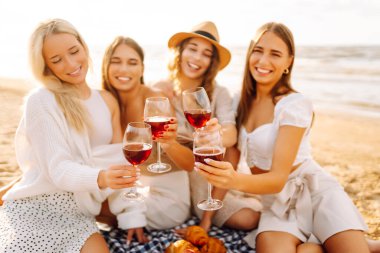 Mutlu kız arkadaşlar gün batımı kumsalında birlikte vakit geçiriyorlar. Ellerinde gözlüklerle dışarıda eğlenen dört güzel kadın. Arkadaşlık kavramı, eğlence. Yaşam biçimi.