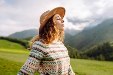 Yeşil tepelere karşı sevimli kadın gezgin özgürlüğü hissediyor. Şapkalı güzel kadın dağlarda güzel bir yerde eğleniyor. Yürüyüş, seyahat, özgürlük kavramı.