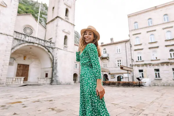 Parlak elbiseli ve şapkalı güzel bir turist eğleniyor ve şehir manzarasının tadını çıkarıyor. Genç bir kadın şehirde geziyor ve eğleniyor. Tatil, tatil, seyahat konsepti.