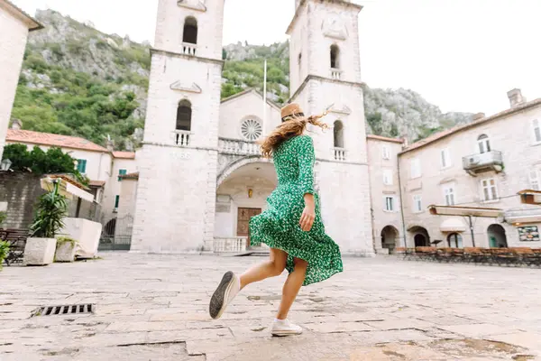 Parlak elbiseli ve şapkalı güzel bir turist eğleniyor ve şehir manzarasının tadını çıkarıyor. Genç bir kadın şehirde geziyor ve eğleniyor. Tatil, tatil, seyahat konsepti.